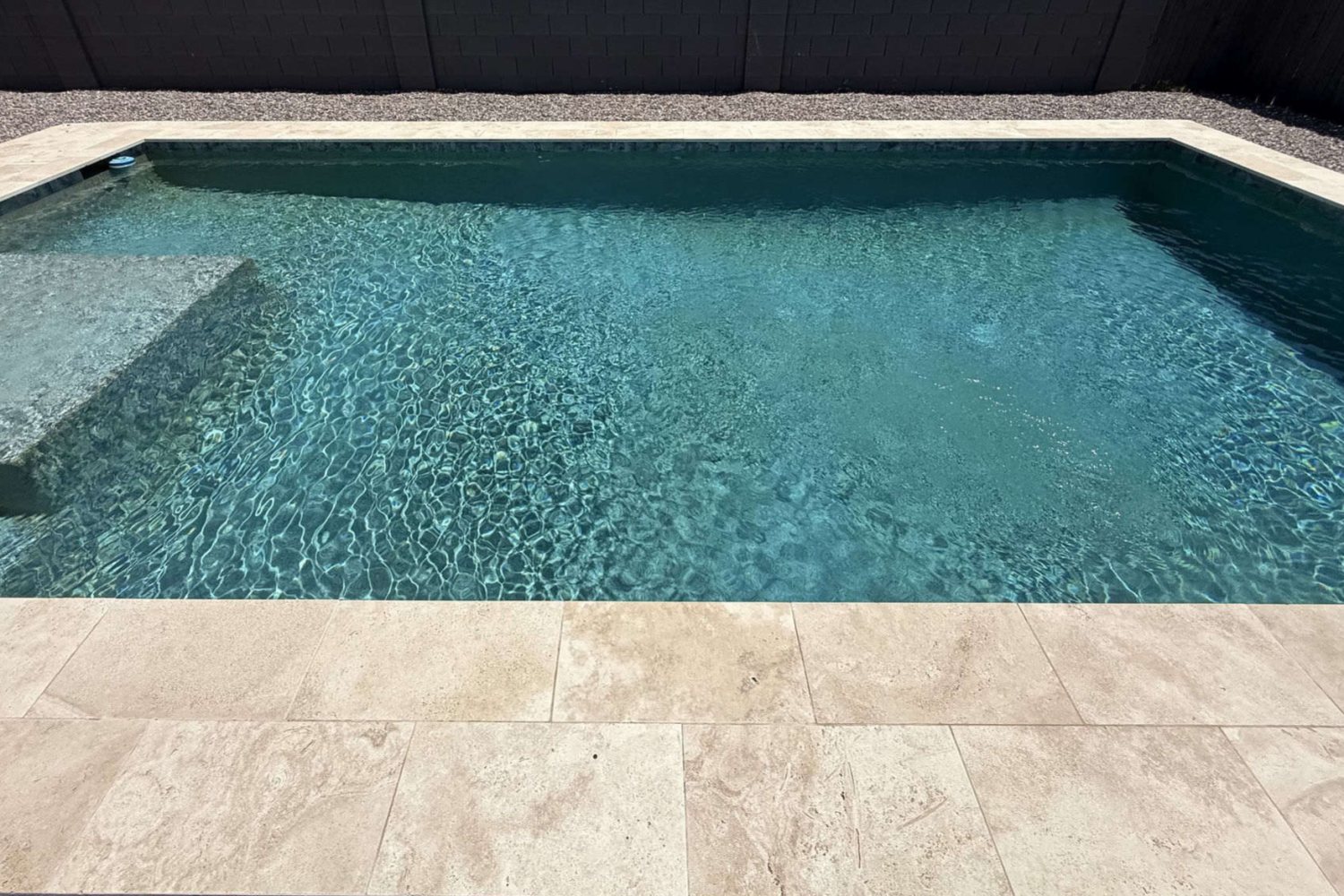 The same pool with clear blue water and a clean travertine deck after Providence Pool Care service