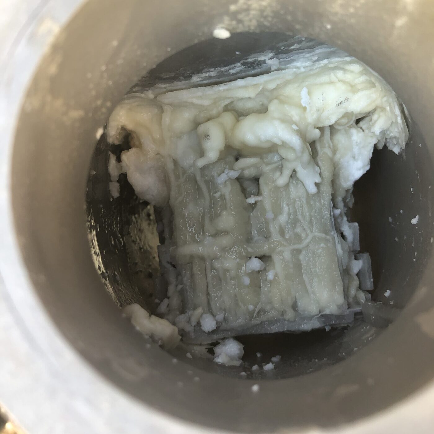 A salt cell fouled solid with thick white calcium deposits, sitting in a cleaning bucket